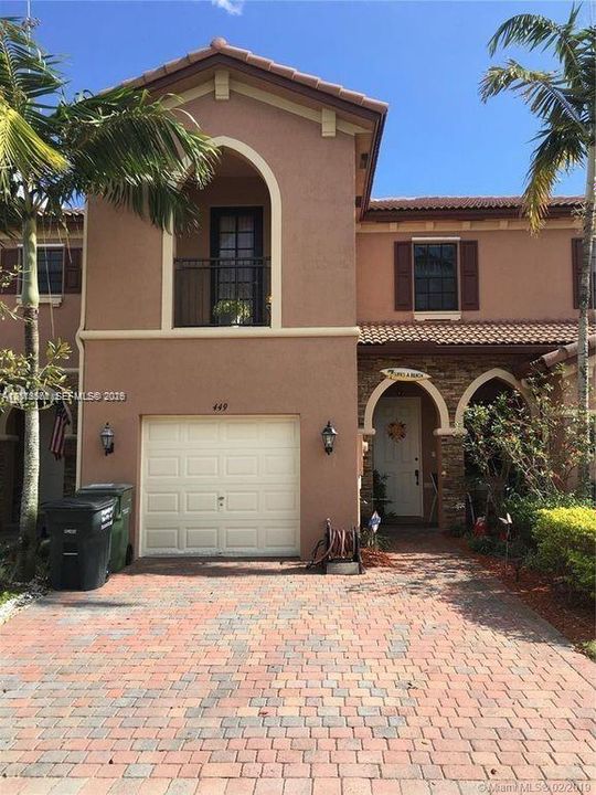 Stucco exterior featuring arched architectural detailing, a clay tile roof, a private balcony with metal railing, and a paved brick driveway