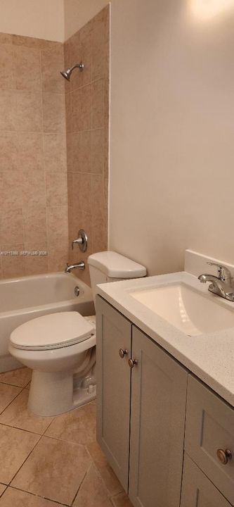 Bathroom featuring a vanity with a light-toned countertop, integrated basin, and cabinet storage, paired with tile flooring and a tiled shower surround