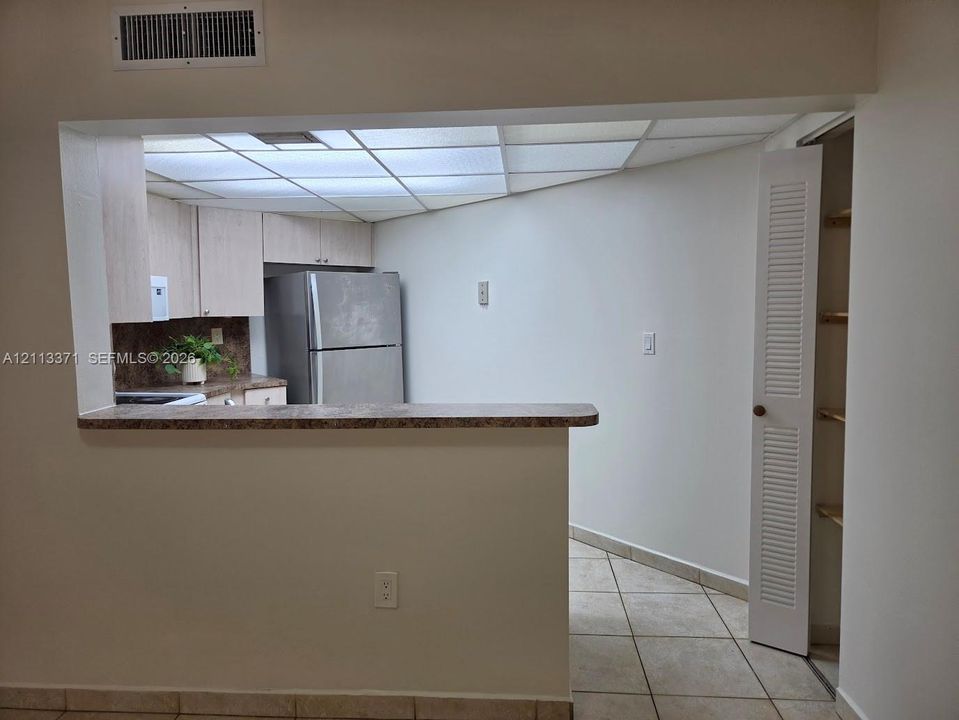 Kitchen featuring light wood-finish cabinetry, a pass-through counter, stainless steel refrigerator, tile flooring, and built-in pantry shelving