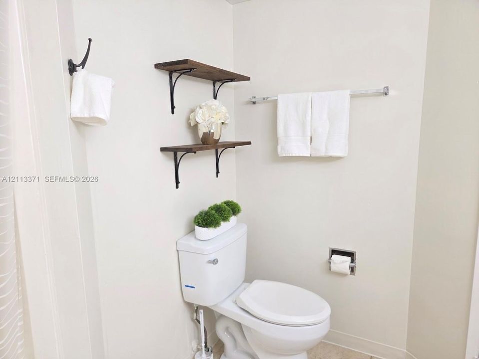 Wall-mounted wood-finish shelving with decorative metal brackets, chrome towel bar, and chrome recessed toilet paper holder