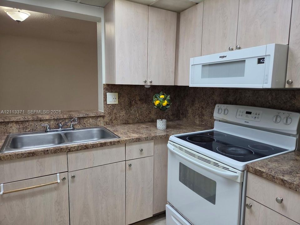 Kitchen featuring light-finish wood cabinetry, laminate countertops, dual-basin stainless steel sink with metal faucet, electric range, and over-the-range microwave