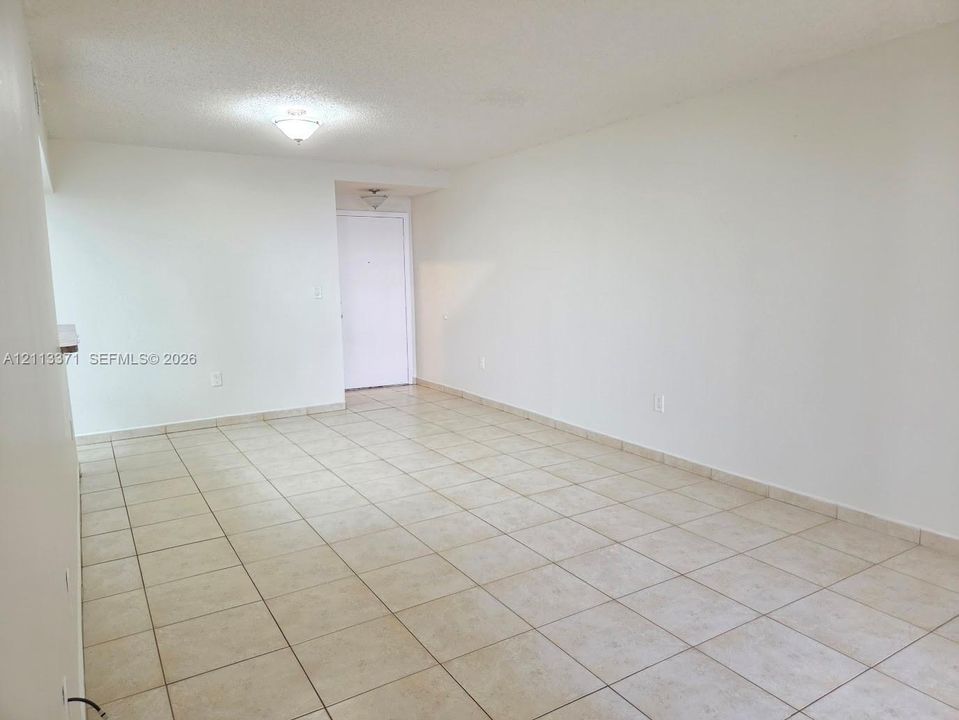 Open interior space featuring light-toned tile flooring, neutral wall paint, and two flush-mount ceiling light fixtures