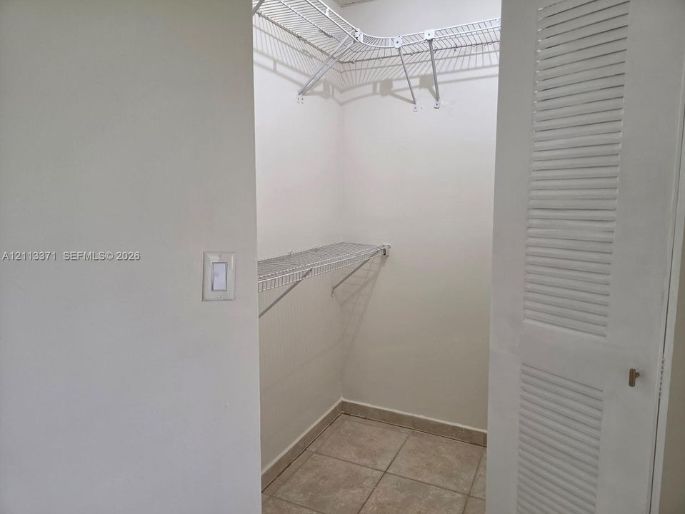 Walk-in closet featuring white louvered doors, tile flooring, and installed wire shelving
