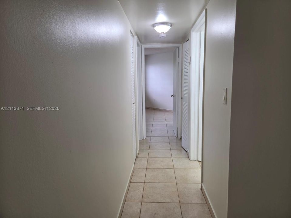 Hallway featuring neutral wall finishes, tile flooring, louvered-panel closet doors, and a ceiling-mounted light fixture