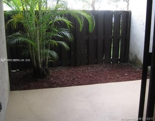 Enclosed patio area featuring a concrete surface, wood-slat privacy fencing, and a mature palm tree set in mulch bedding
