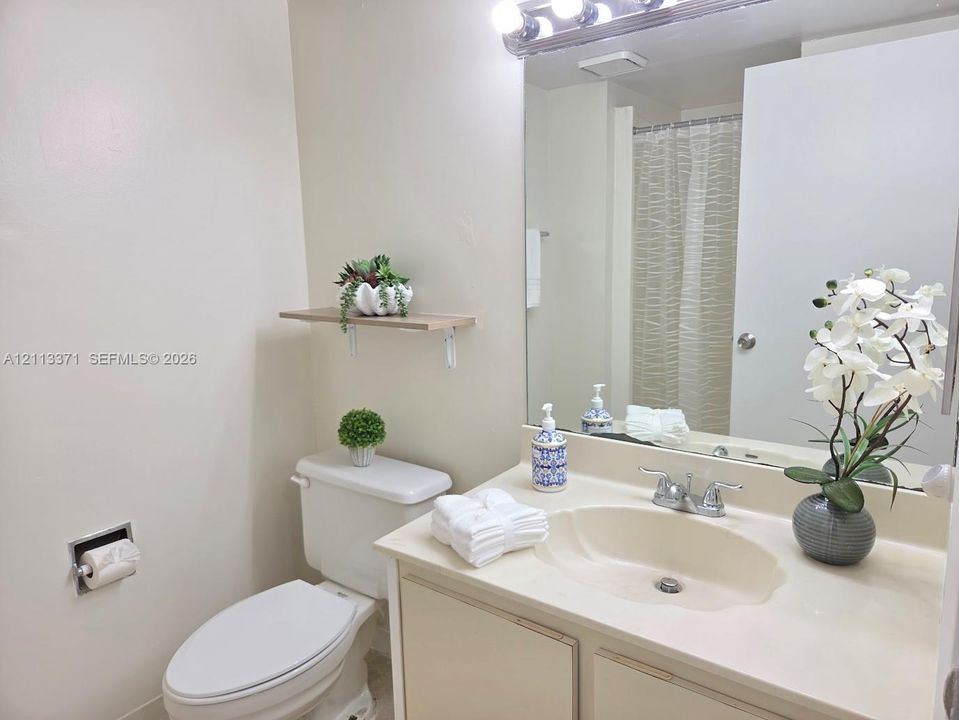 Bathroom featuring a vanity with an integrated basin, a large wall-mounted mirror, a four-light fixture, and a floating wall shelf