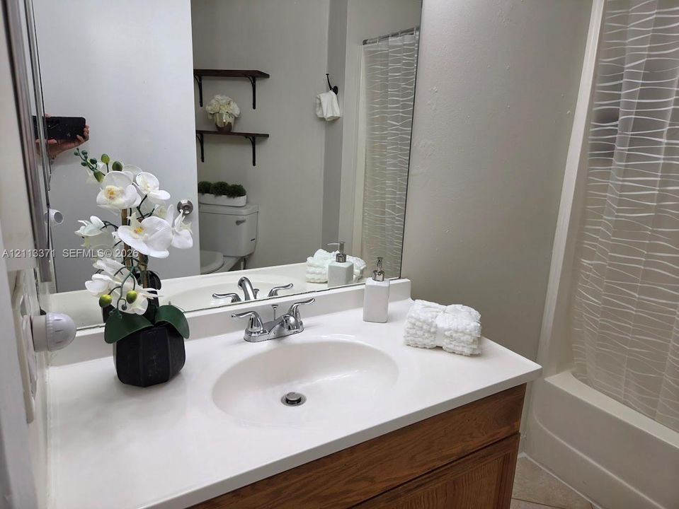Bathroom vanity featuring a solid surface countertop, integrated sink, wood-finish cabinetry, full-width wall mirror, and wall-mounted shelving