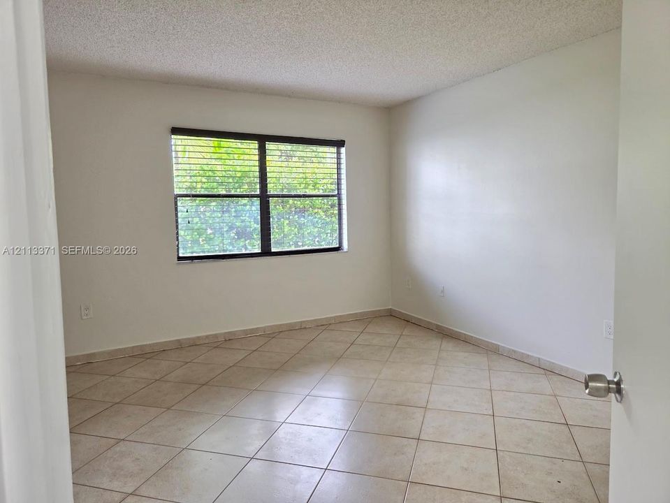 Neutral-toned ceramic tile flooring, clean white wall finishes, and a single-pane window with dark-frame horizontal blinds