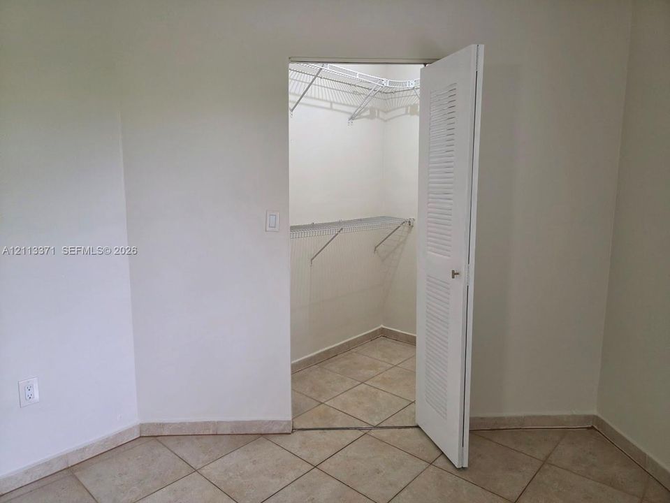 Walk-in closet featuring white louvered door, tile flooring, and built-in wire shelving