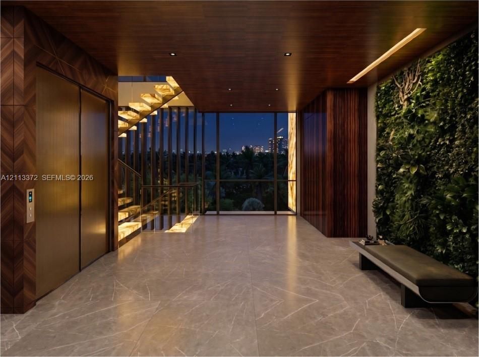 Grand entrance hall featuring large-format stone flooring, a living plant wall, integrated metal elevator doors, wood-paneled ceilings with recessed lighting, and a floating staircase with glass railings
