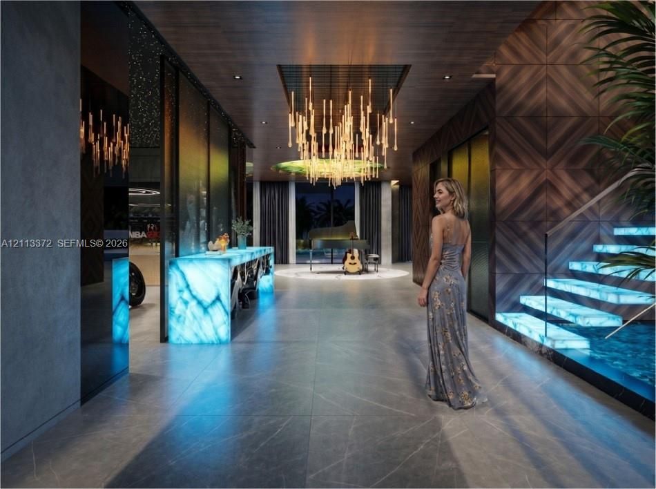 Entry hall featuring large-format tile flooring, illuminated stone accents, wood-paneled walls, custom tiered chandelier, and a floating staircase with glass railings