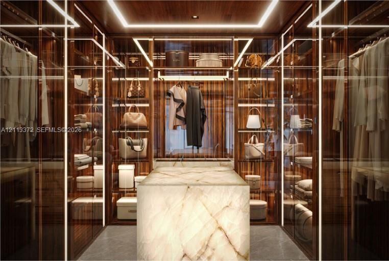 Custom walk-in closet featuring floor-to-ceiling wood cabinetry, integrated linear LED lighting, glass-fronted storage displays, and a central stone island with a polished finish