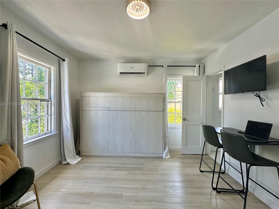 Neutral-toned room featuring wood-finish flooring, a wall-mounted ductless air conditioning unit, a built-in cabinet, and multi-pane windows with hardware