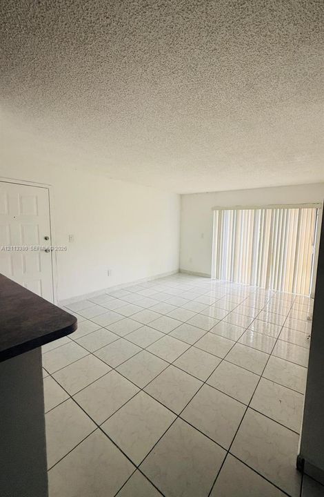 Interior space featuring large-format ceramic tile flooring, a six-panel entry door, and vertical blind window treatments