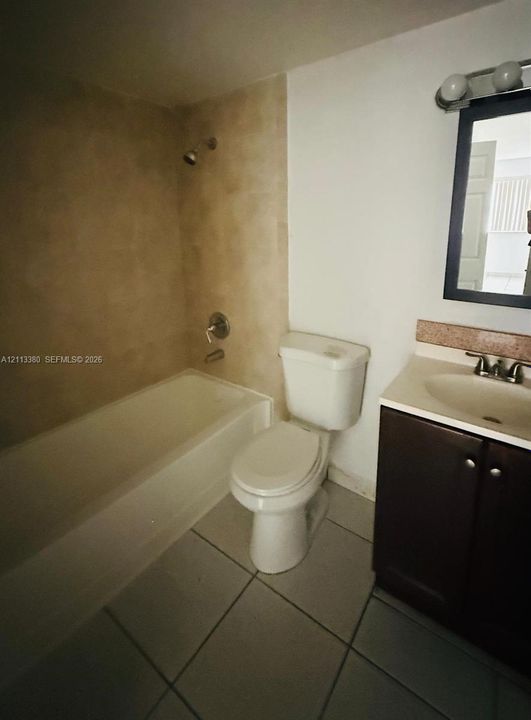 Full bathroom featuring a tub-shower combination with tile surround, a dark-finish wood vanity with a solid surface countertop, ceramic tile flooring, and a framed wall-mounted mirror