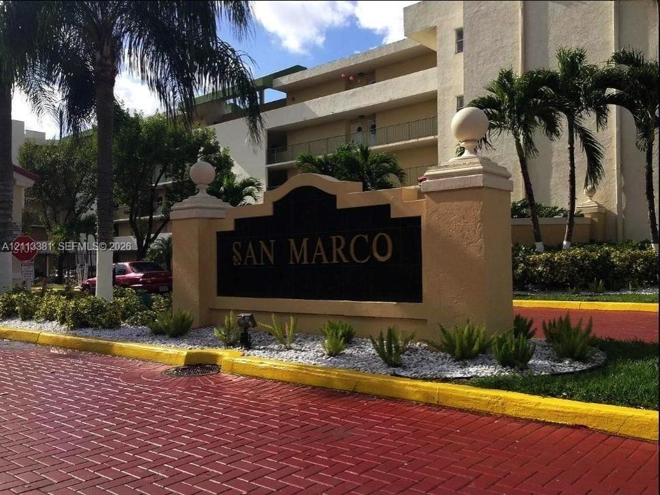Stucco monument sign featuring ball finials and low-maintenance landscaping with decorative stone ground cover, finished with red brick paver surfacing