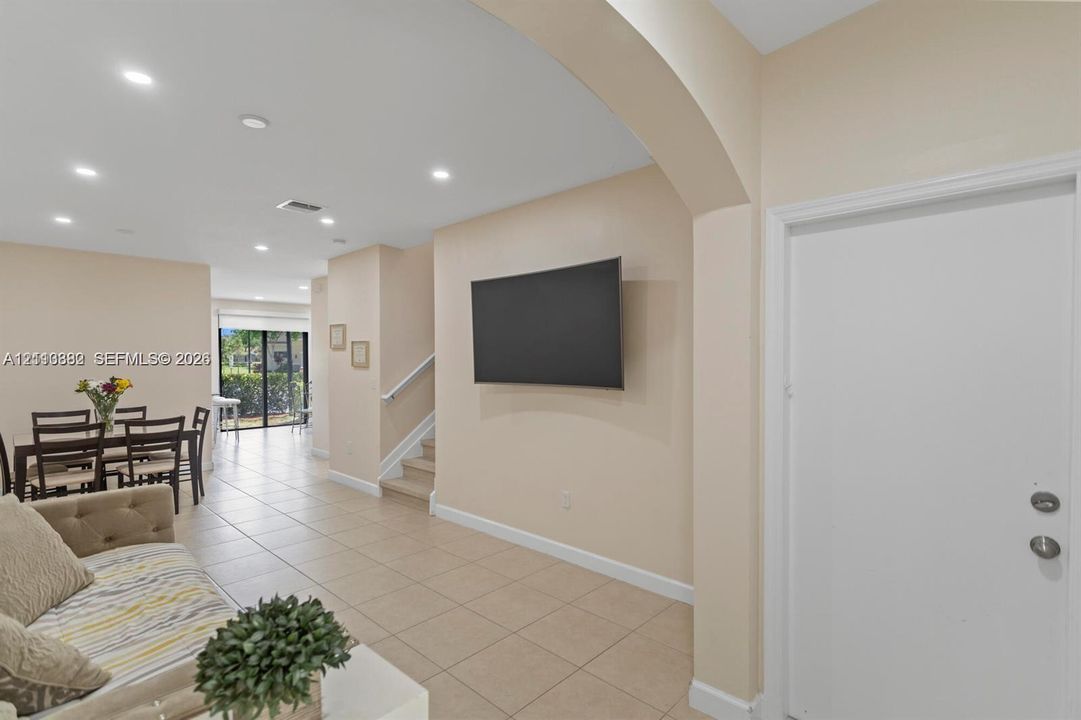 Interior space featuring neutral-toned tile flooring, recessed ceiling lighting, a curved architectural archway, and a staircase with a white handrail