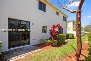 Stucco exterior featuring a sliding glass door, a brick paver patio, and mature landscaping
