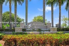 Community entrance signage featuring masonry pillar accents, decorative landscaping, and mature palm trees