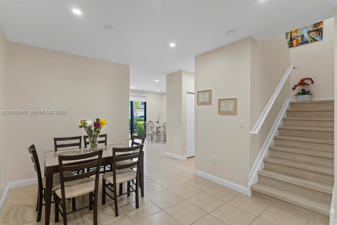 Neutral-toned interior space featuring light-colored tile flooring, recessed ceiling lighting, a staircase with wood-finish treads, and a white handrail