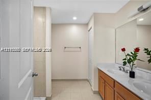 Bathroom featuring a dual-sink vanity with a solid-surface countertop, full-width mirror, tile flooring, and a tiled shower enclosure