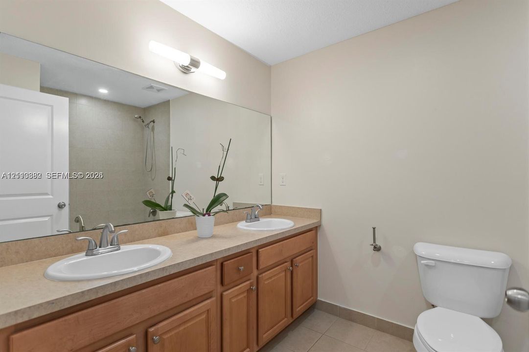 Double vanity featuring solid-surface countertops, dual drop-in sinks with chrome hardware, wood cabinetry, and a full-width wall mirror