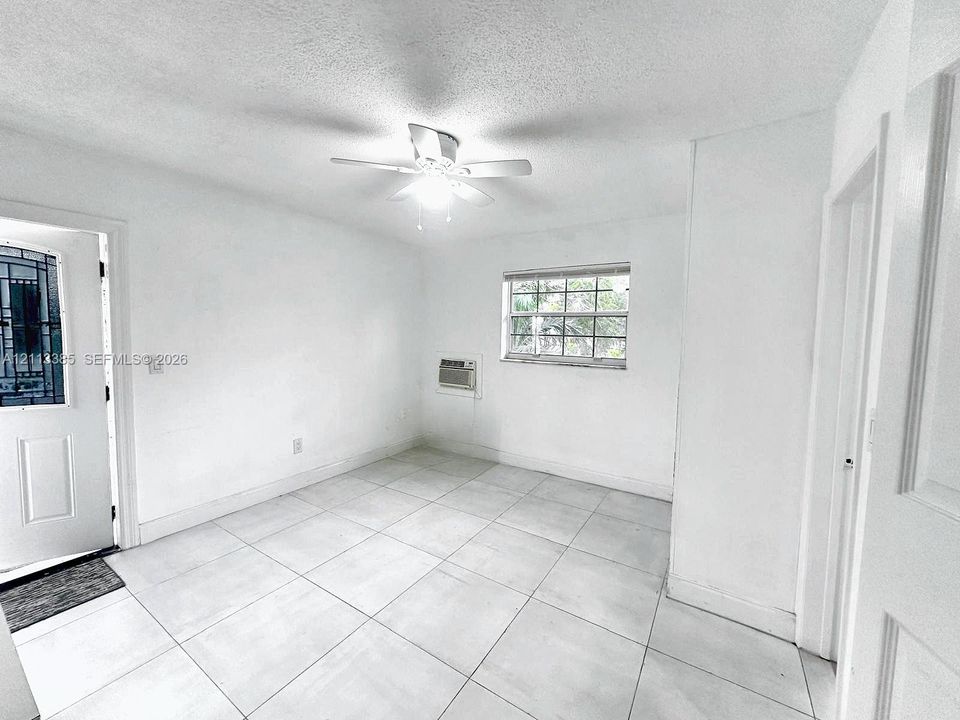 Large-format tile flooring, ceiling fan with integrated lighting, multi-pane window, and wall-mounted air conditioning unit