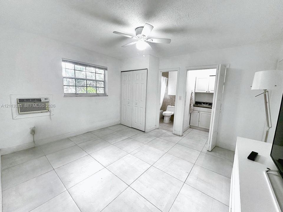 Large-format tile flooring, ceiling fan with light fixture, built-in closet with double doors, and window with security bars