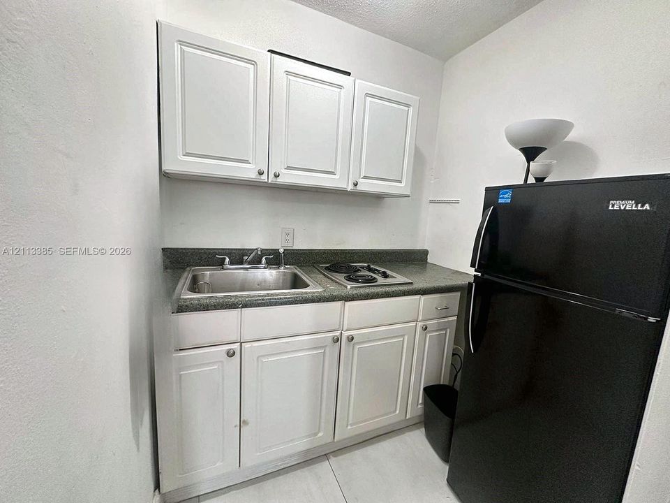 Kitchenette featuring white Shaker-style cabinetry, stone-finish countertops, stainless steel sink with metal faucet, and an integrated two-burner electric cooktop