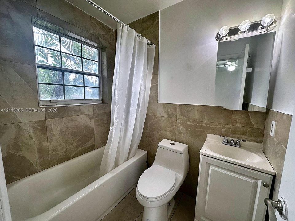 Bathroom featuring large-format neutral wall tile, integrated tub and shower combination, vanity with an inset basin, dual-handle faucet, and three-bulb vanity lighting