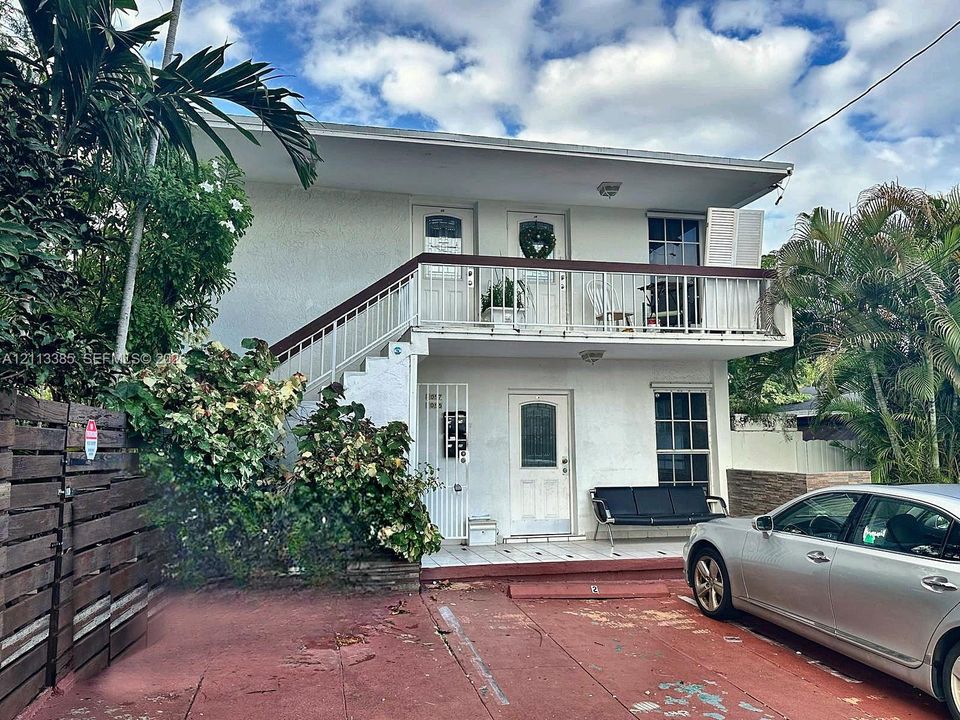Two-story exterior featuring white stucco siding, a metal railed balcony, and a dedicated paved parking area