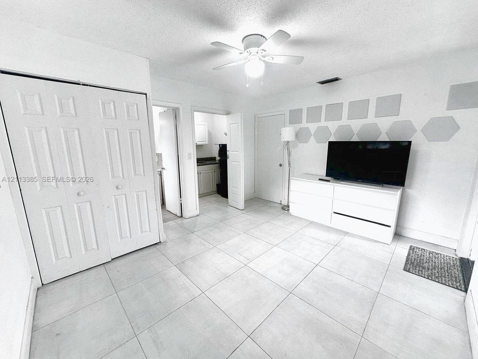 Interior space featuring large-format neutral tile flooring, white six-panel bi-fold closet doors, and a ceiling-mounted light fixture with integrated fan