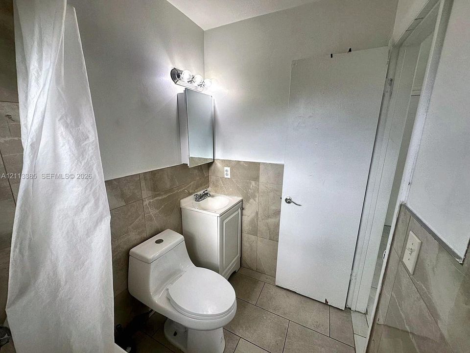 Bathroom featuring large-format neutral wall and floor tiling, a vanity with a white rectangular sink, a mirrored medicine cabinet, and a three-light wall-mounted fixture