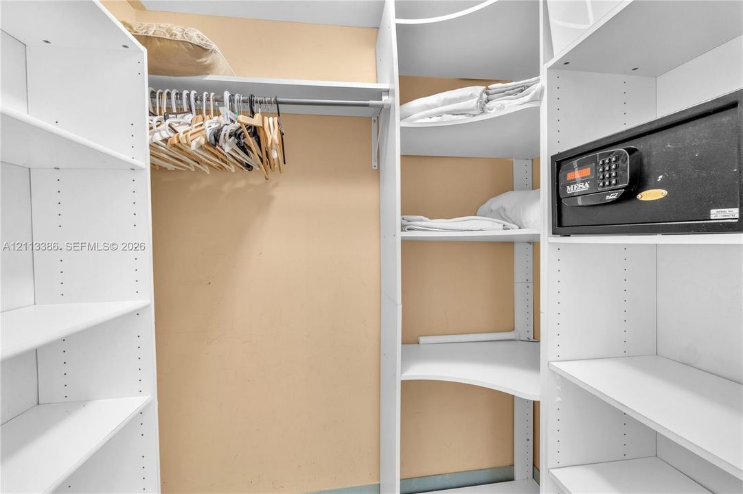 Walk-in closet featuring white floor-to-ceiling built-in shelving, adjustable storage cubbies, a hanging rod, and a built-in security safe