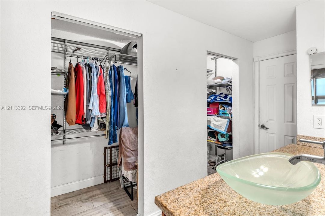 Vanity featuring a stone countertop, glass vessel sink, and chrome faucet, accompanied by walk-in closets with integrated wire shelving and wood-finish flooring