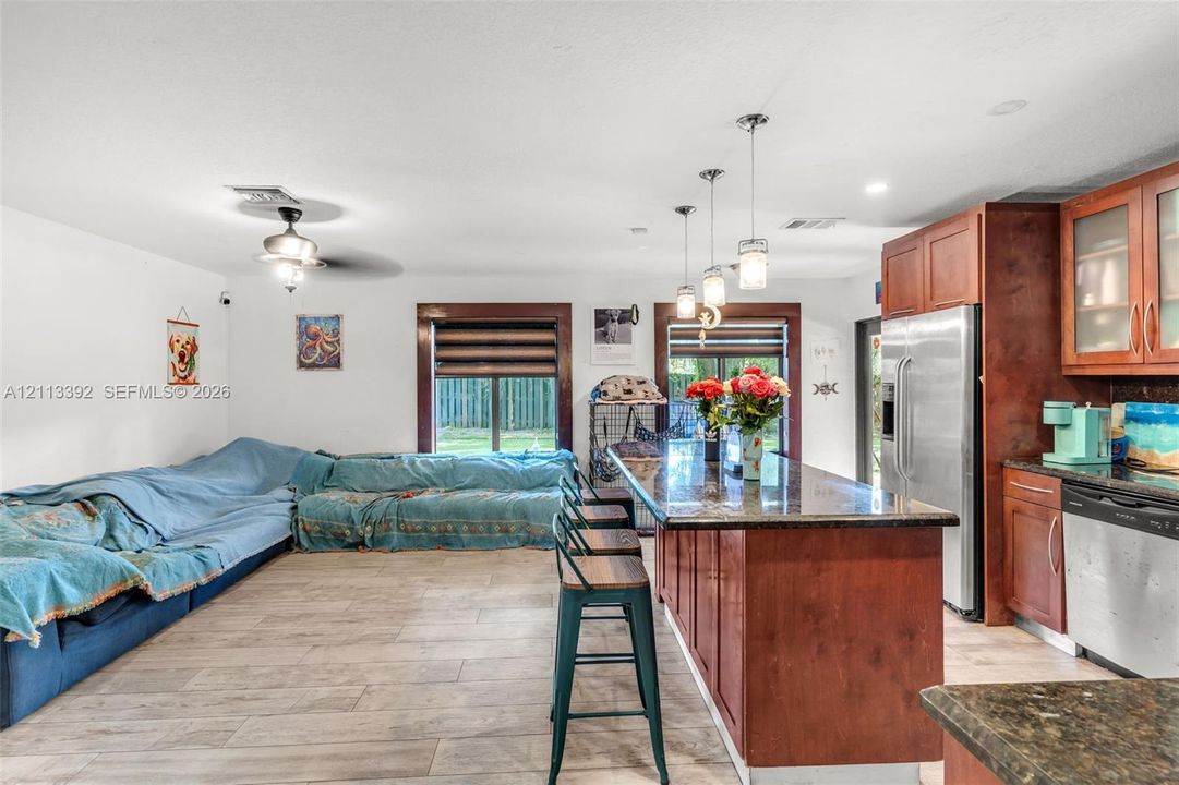 Open-concept kitchen featuring stained wood cabinetry, stone countertops, stainless steel appliances, pendant lighting, and wood-finish flooring