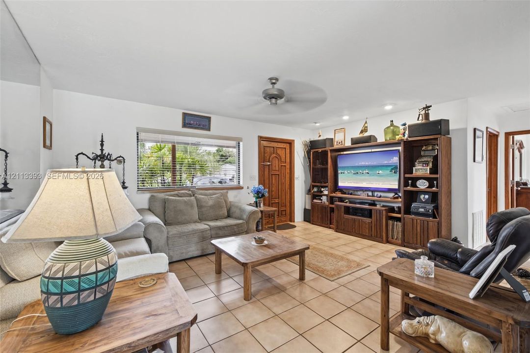 Living area featuring neutral tile flooring, wooden media cabinetry, a solid wood front entry door, and a ceiling fan