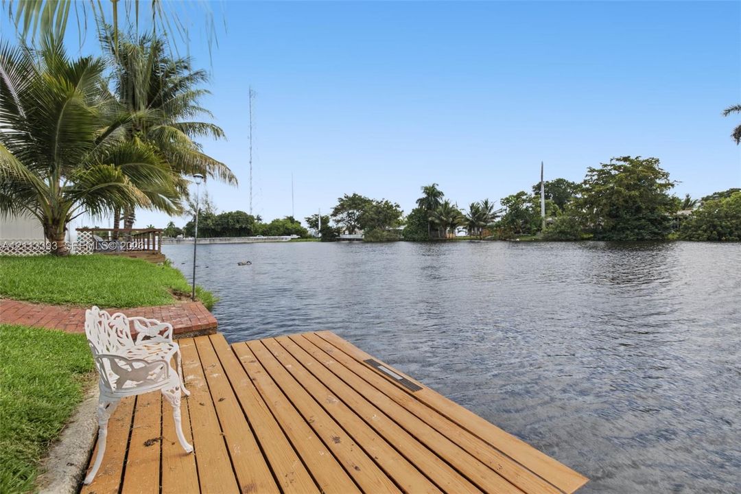 Waterfront lot featuring a wooden dock, brick paver pathway, and mature palm trees