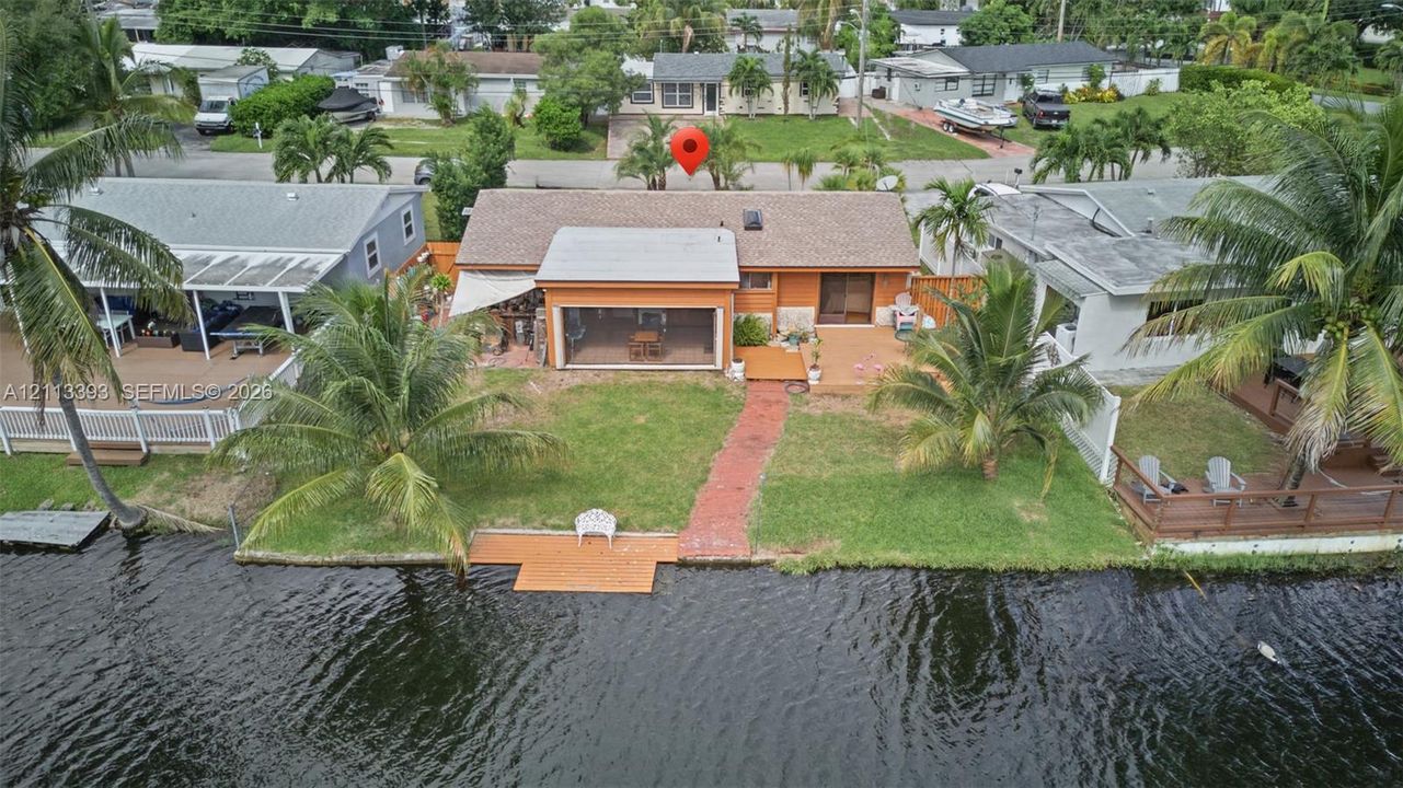 Waterfront residence featuring a screened-in lanai, wood-finish decking, a paved walkway, and direct water access with a private dock