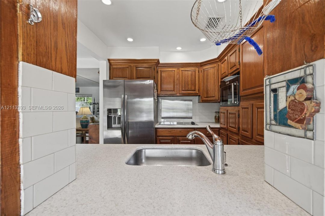 Kitchen featuring recessed lighting, medium-tone wood cabinetry, stainless steel refrigerator, white subway tile backsplash, and quartz countertop with a stainless steel undermount sink