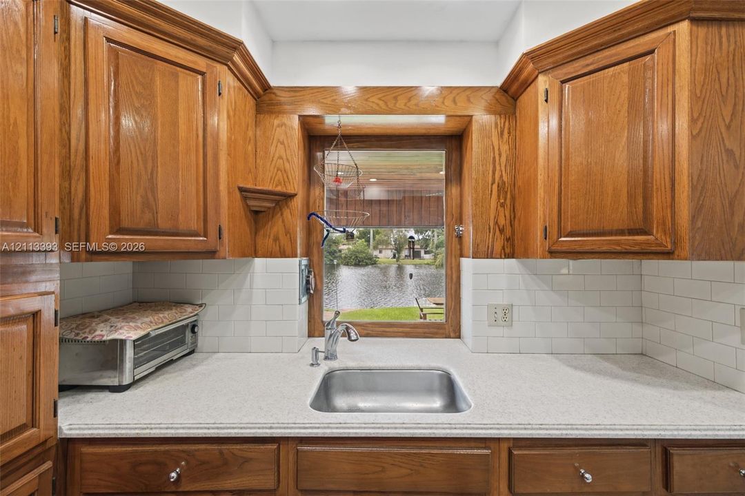 Kitchen featuring custom wood cabinetry, a stainless steel undermount sink with a gooseneck faucet, light-toned solid surface countertops, and white subway tile backsplash