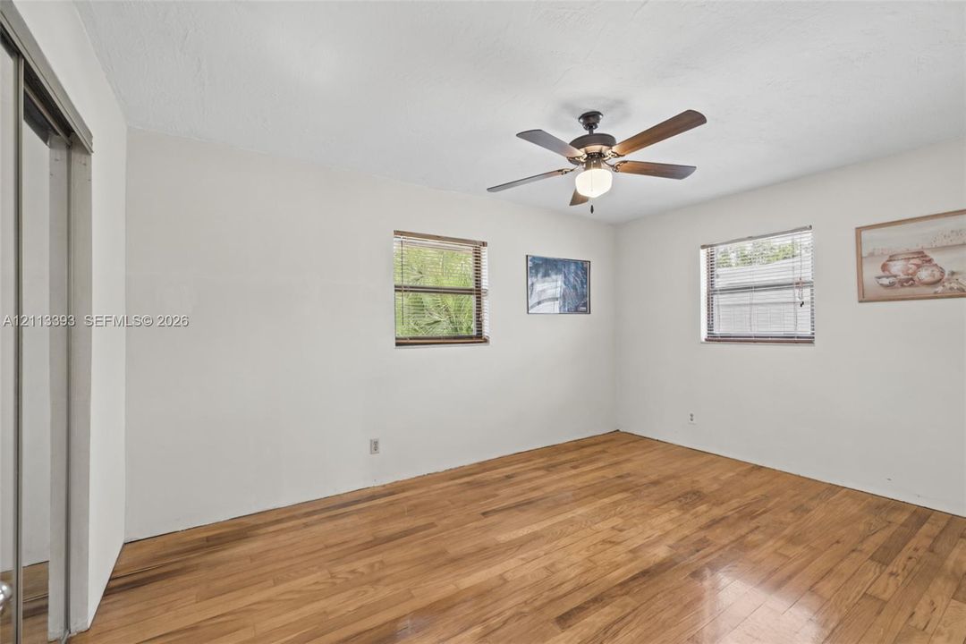 Room featuring wood-finish flooring, two windows with horizontal blinds, a ceiling-mounted fan with integrated light, and a sliding mirrored closet door