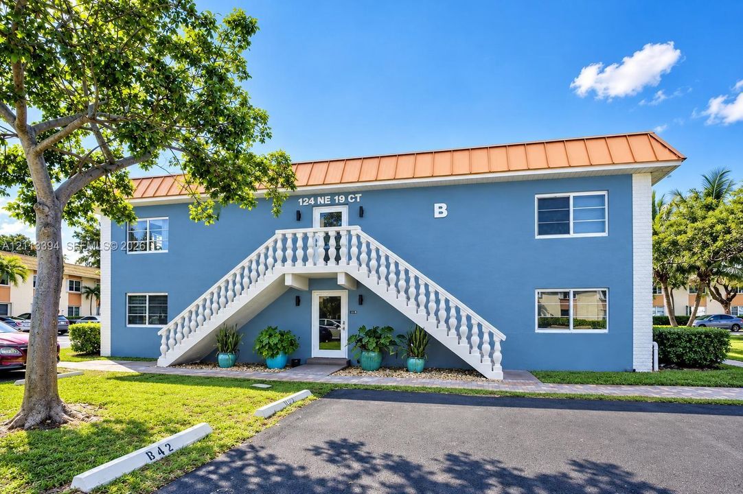 Two-story exterior featuring a metal roof, stucco finish, exterior staircase with balustrade railings, and paved walkways