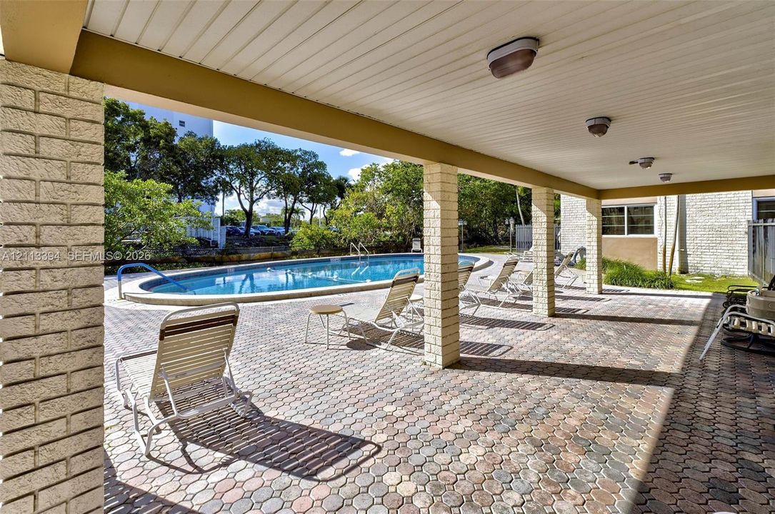 Covered patio featuring brick-paver flooring and structural brick columns, opening to a swimming pool with a concrete pool deck