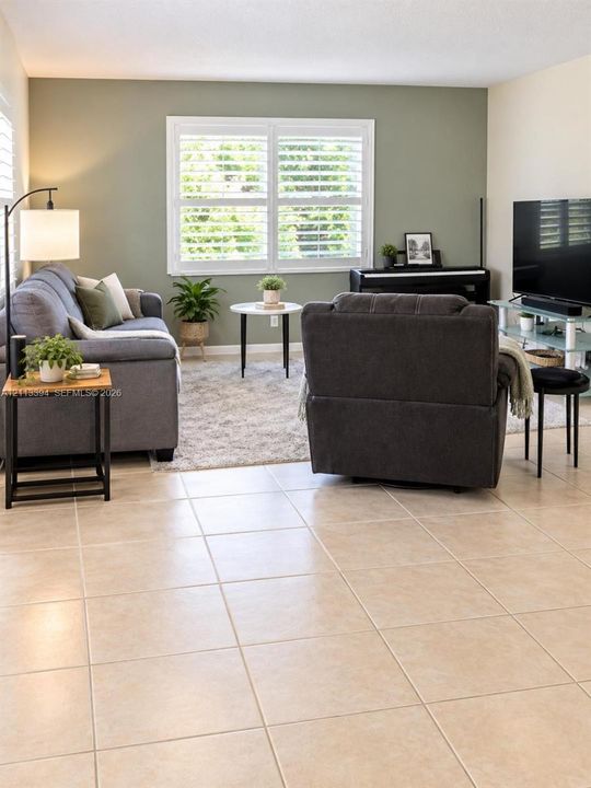 Neutral-toned tile flooring, sage green accent wall, and plantation shutters