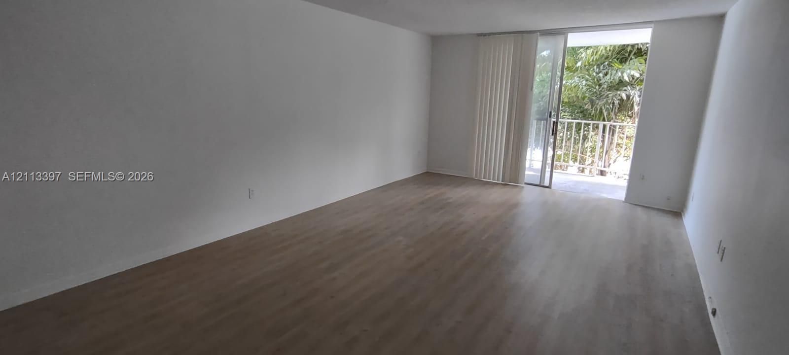 Open-concept living space with neutral wall paint, wood-finish flooring, and a sliding glass door providing access to a private balcony
