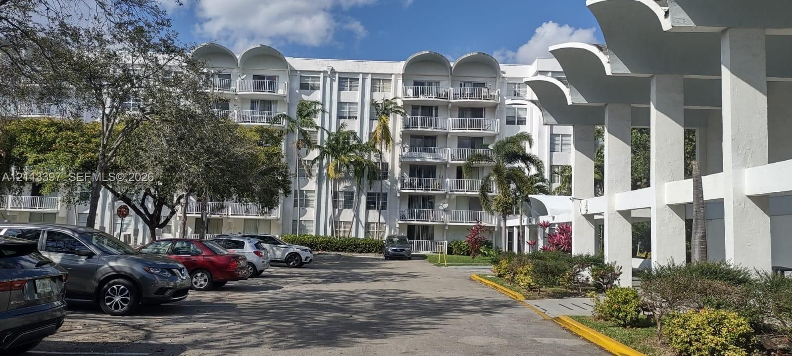 Multi-story residential building featuring arched architectural roof detailing, private balconies with metal railings, and a covered ground-level portico