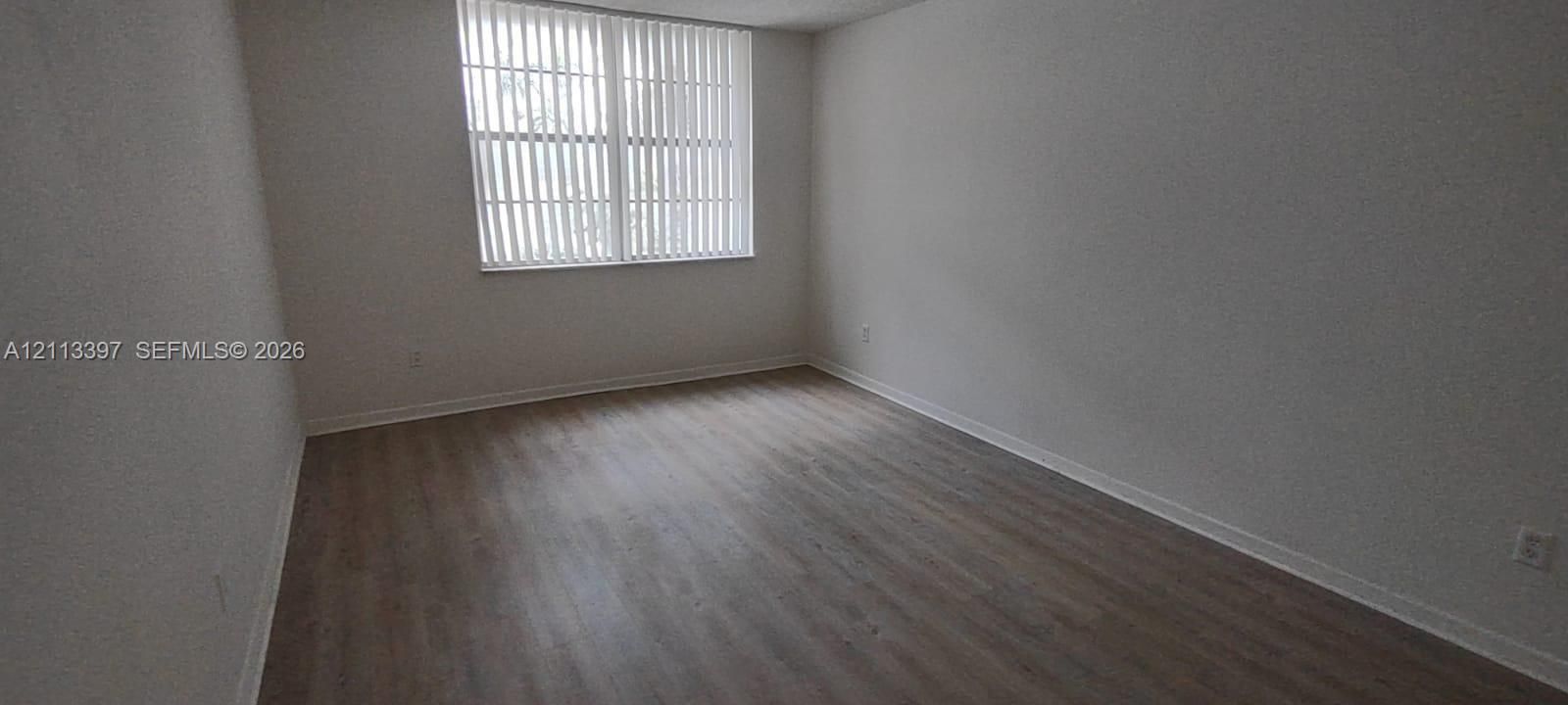 Interior room featuring wood-finish flooring, neutral walls, and a large window with vertical blinds