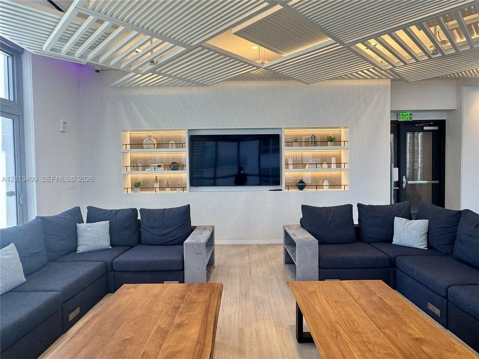 Geometric slatted ceiling design featuring recessed lighting, custom built-in wall shelving with integrated illumination, and wood-finish flooring