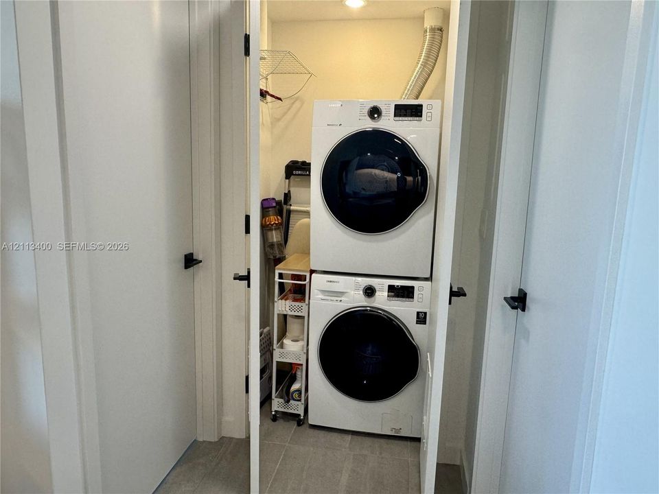 Laundry closet featuring stacked high-efficiency washer and dryer, tile flooring, and matte black door hardware